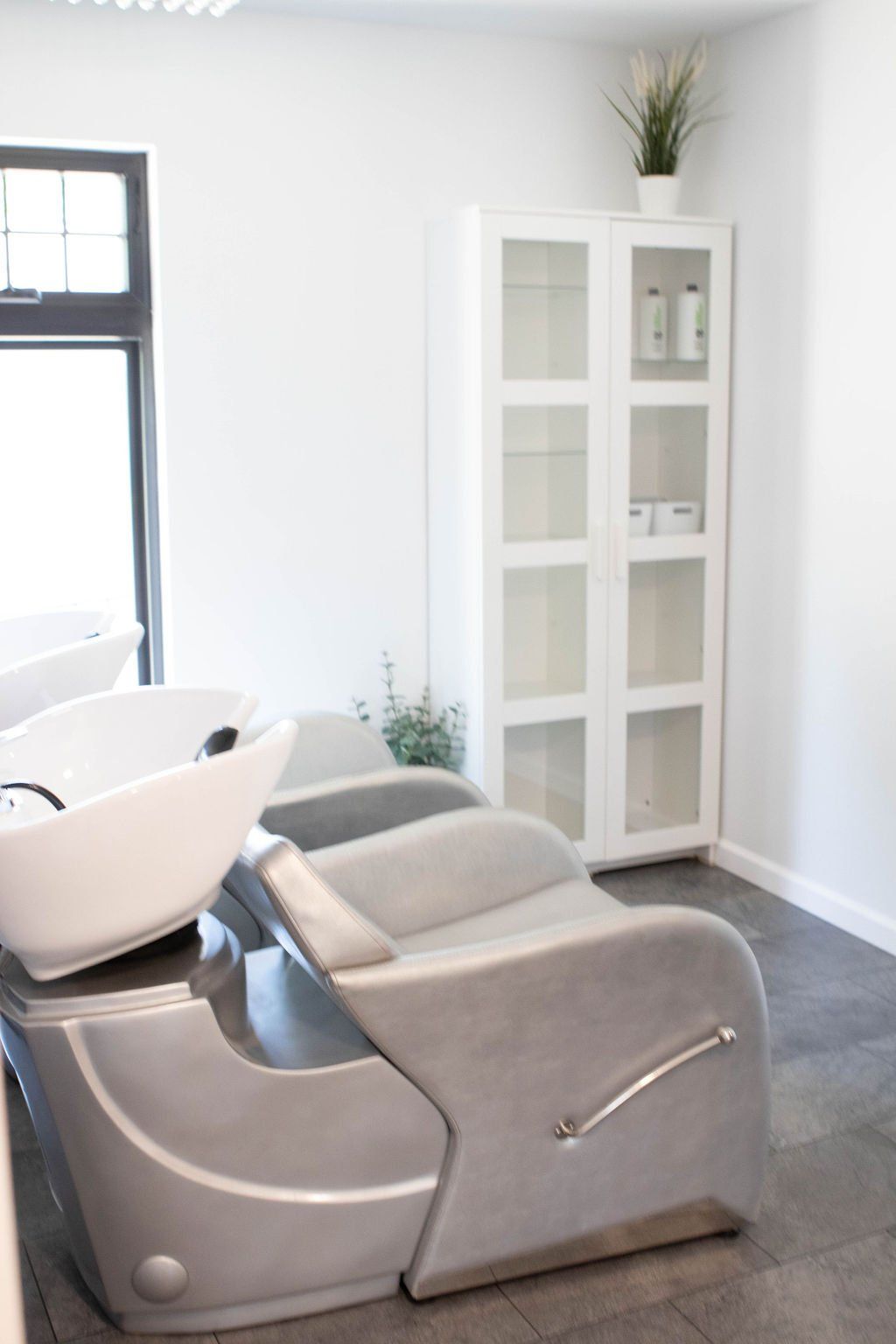 Hair salon interior with a shampoo chair, sink, cabinet, and greenery.