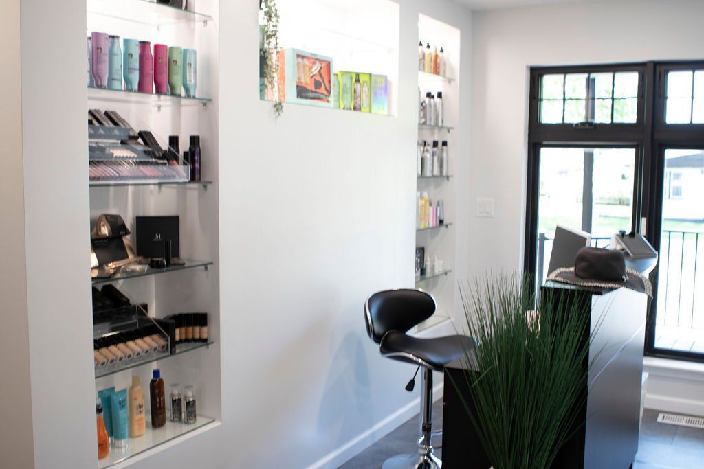 Salon interior with product display shelves, a black reception desk, and a stool.