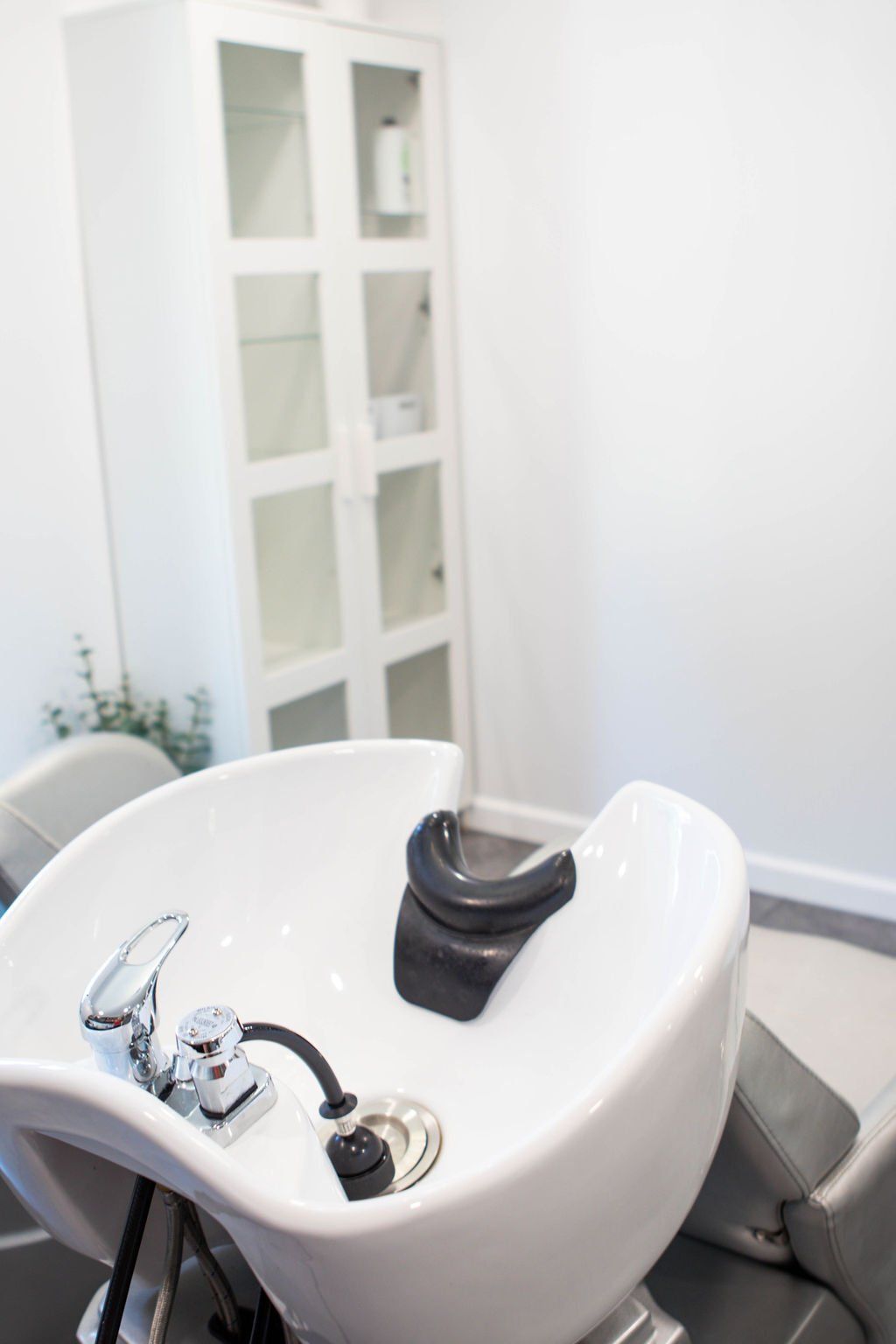 White salon sink with neck rest, chrome faucet, and cabinet in a bright room.