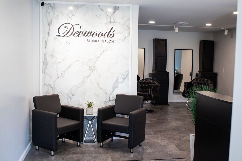 Salon waiting area with two black chairs, marble wall backdrop, and salon stations.