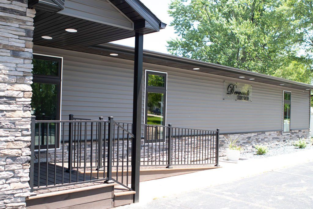 Building with stone facade and gray siding, black railings, and windows.
