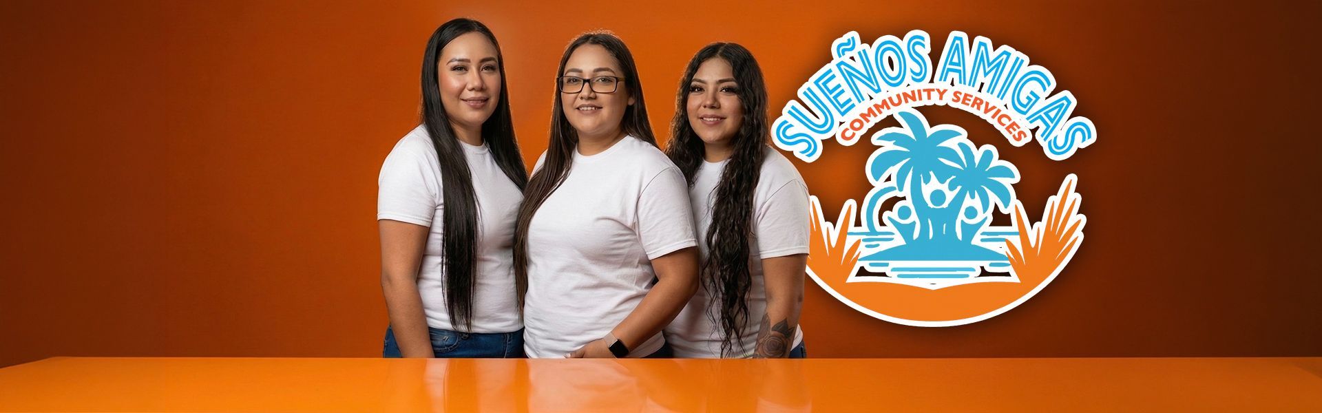 Three people in white t-shirts stand before an orange wall featuring the 
