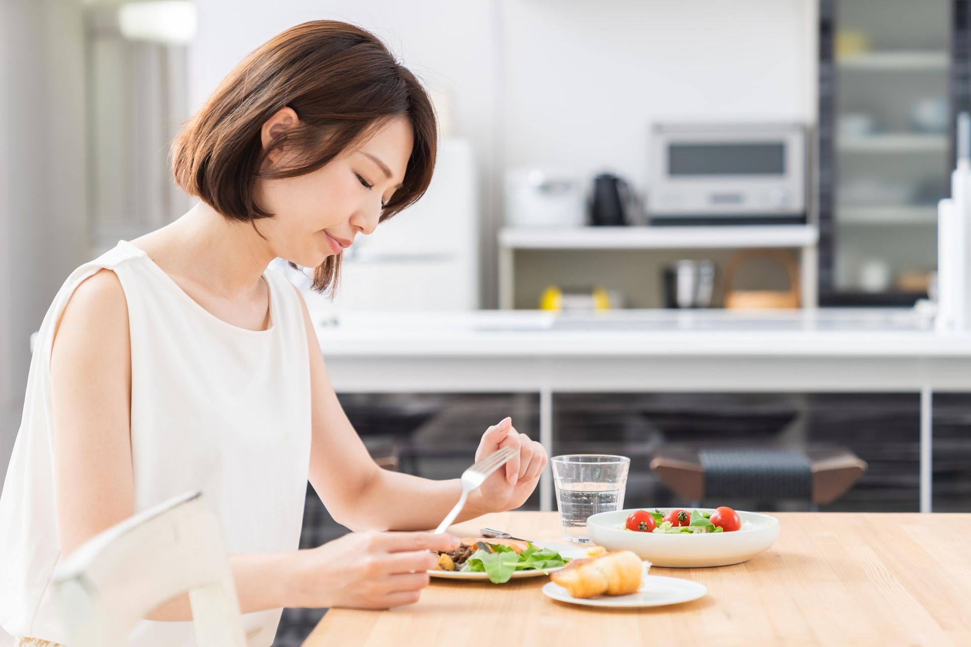 Woman eating at a table, with salad and water; kitchen in background.
