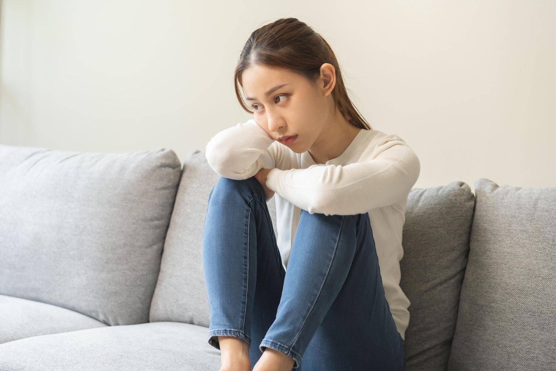 Woman sitting on a couch, looking sad with arms around legs.