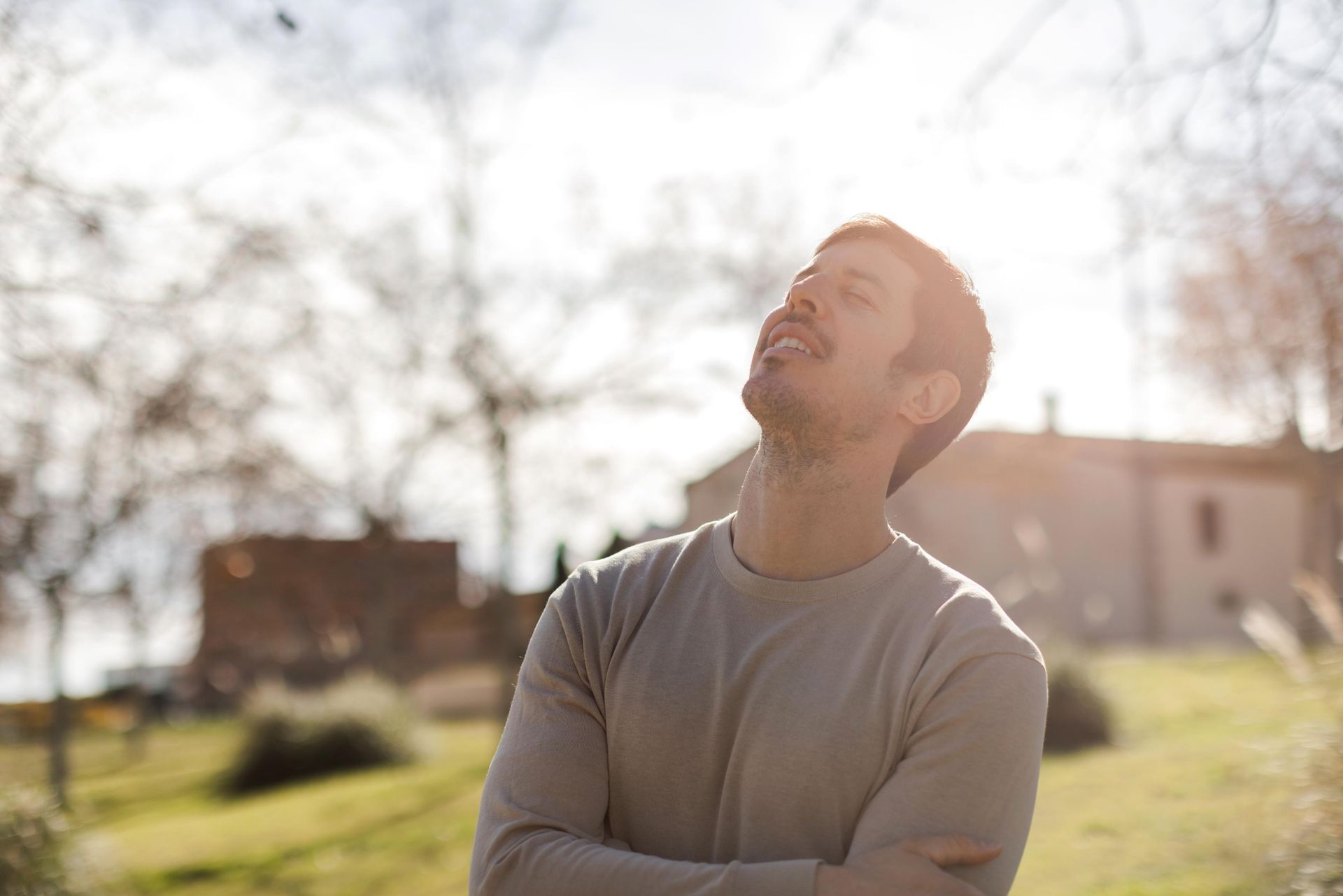 Man looking upward with eyes closed, sun shining on his face outdoors.