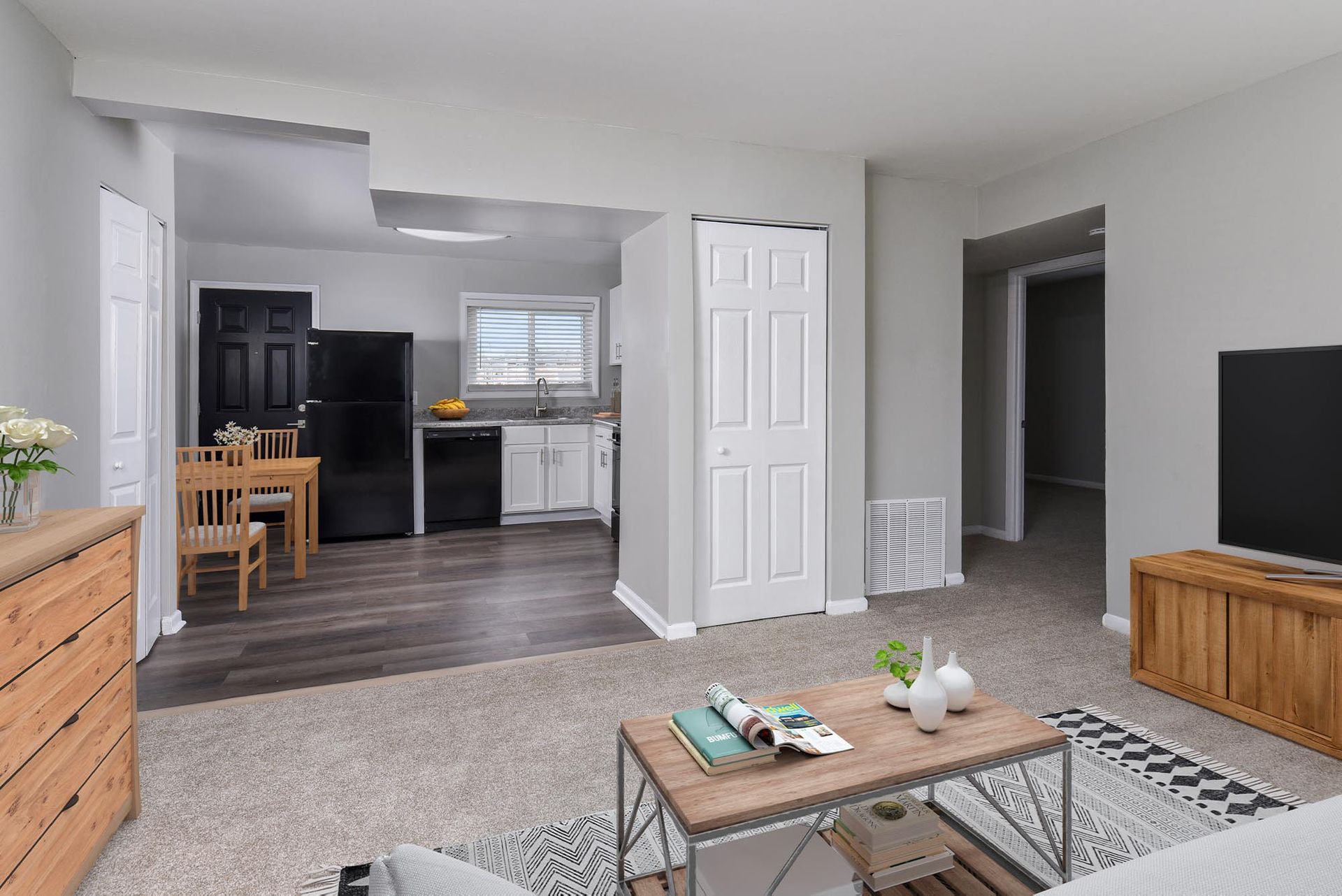 Open-concept living area with beige carpet, coffee table, TV, and white kitchen cabinets.