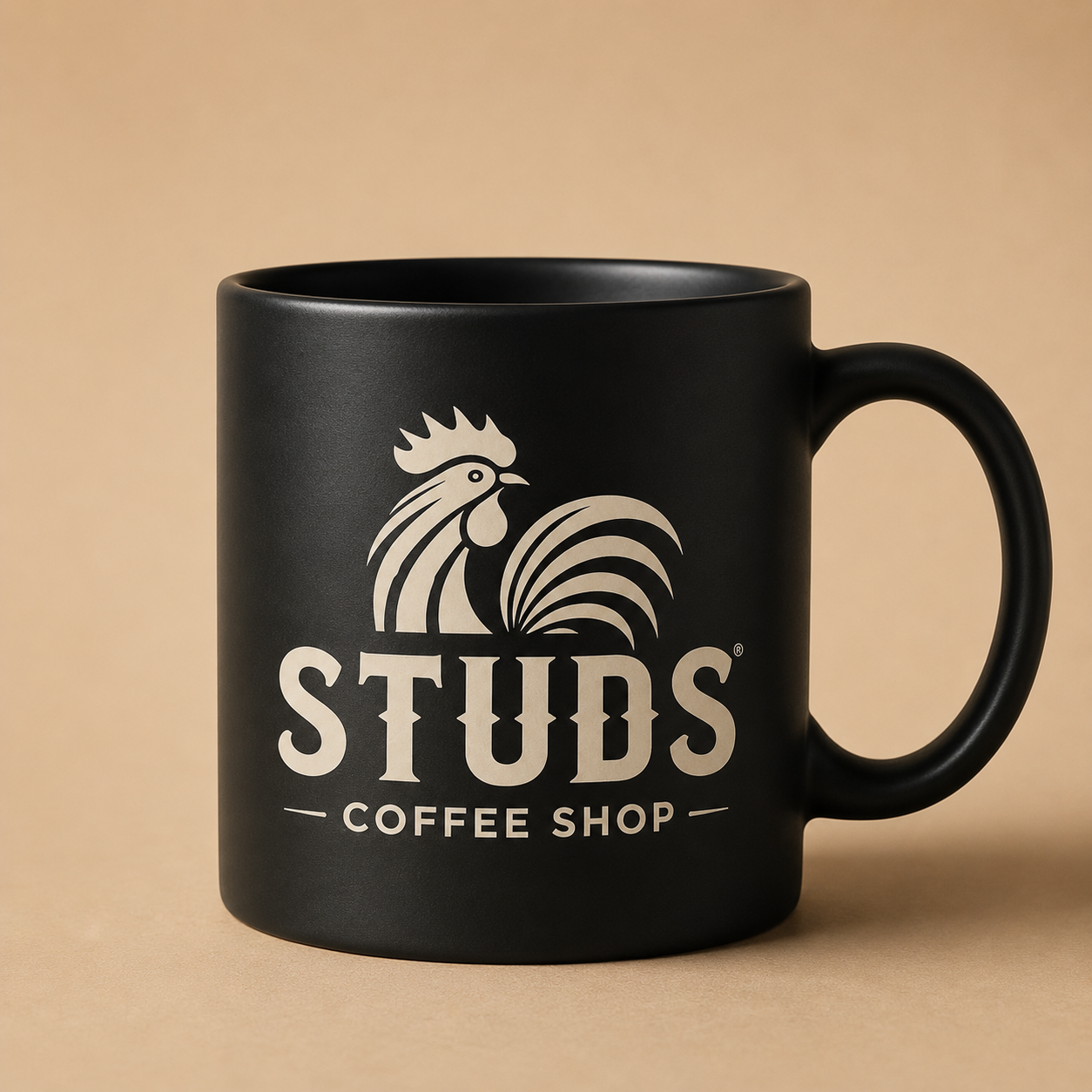 Black mug with rooster logo and “STUDS Coffee Shop” text on a tan background
