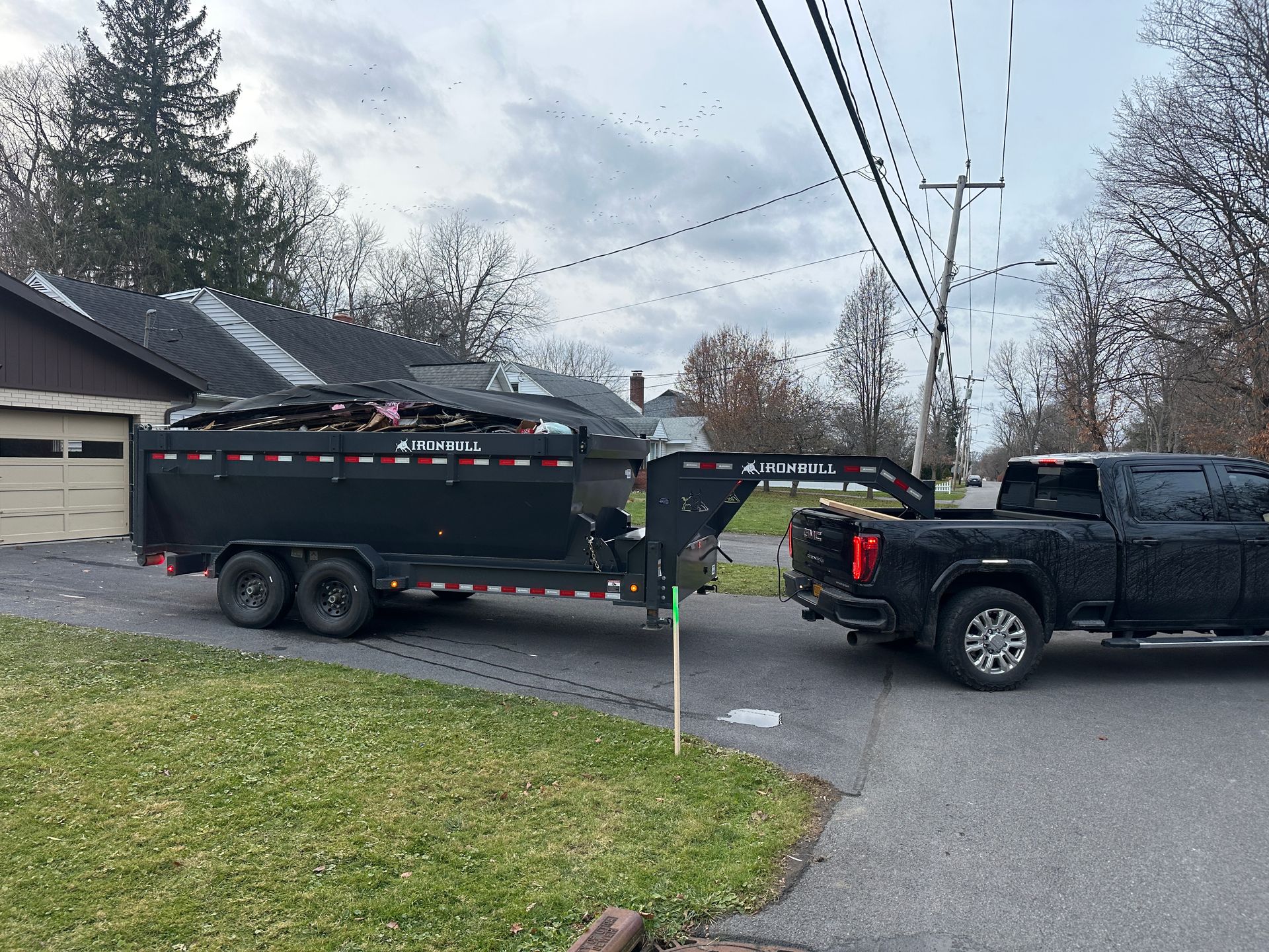 A black truck is towing a dump trailer down a street.