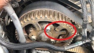 Close-up of a car engine's timing belt and camshaft gear. A section of the gear is highlighted in red.