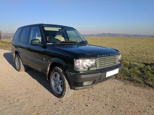 Dark green Range Rover SUV parked on a dirt road in a field with a clear sky.