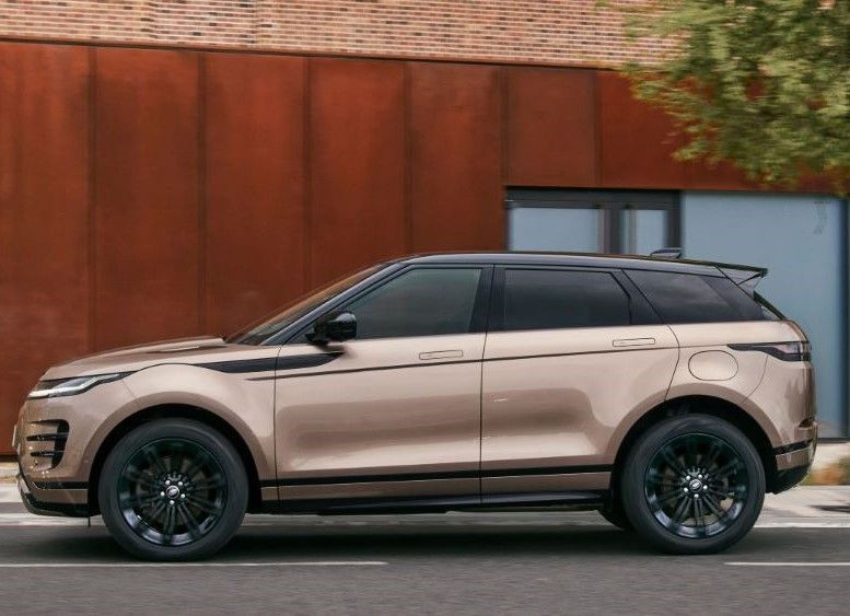 A bronze Range Rover SUV parked on a street in front of a rusty brown building with a black roof and wheels.