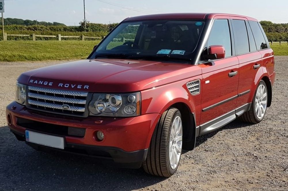 Red Range Rover Sport SUV parked on a paved surface. Sunny day.
