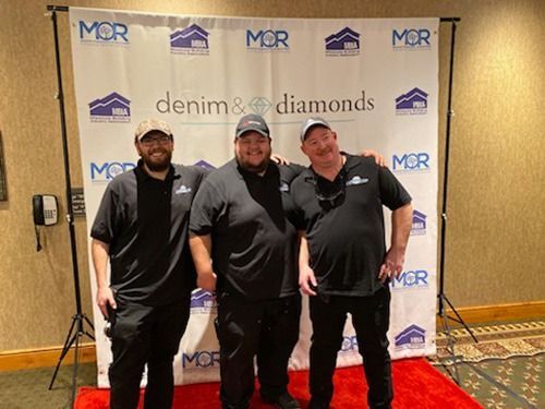 Three men are posing for a picture in front of a denim and diamonds backdrop.