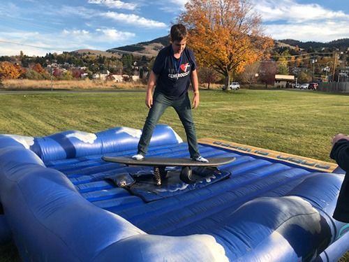 A boy is riding a skateboard on top of an inflatable wave machine.