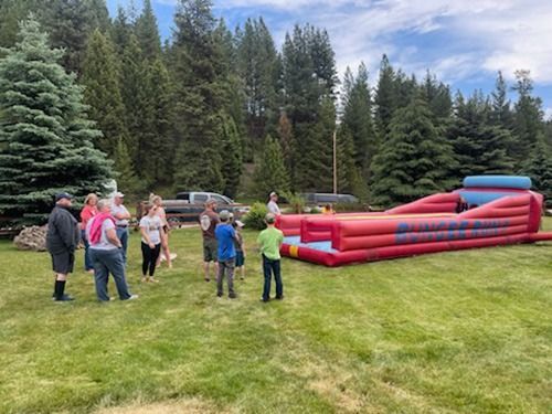 A group of people are standing in a grassy field in front of a bouncy house.