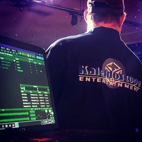 A man wearing a kaleidoscope entertainment shirt looks at a computer screen