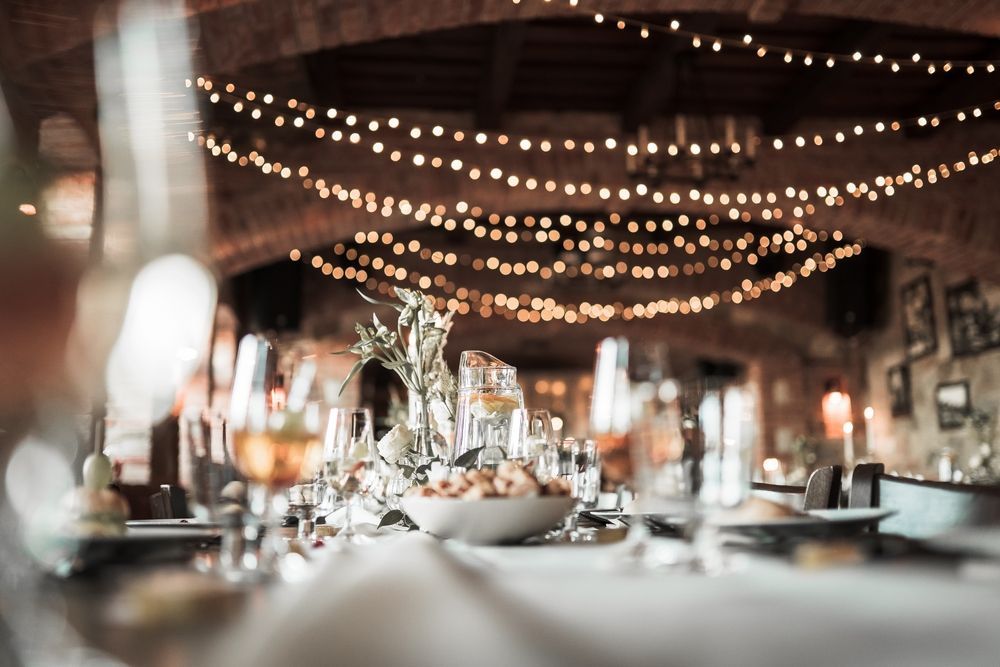 A table set for a wedding reception with plates , glasses , and a bowl of food.