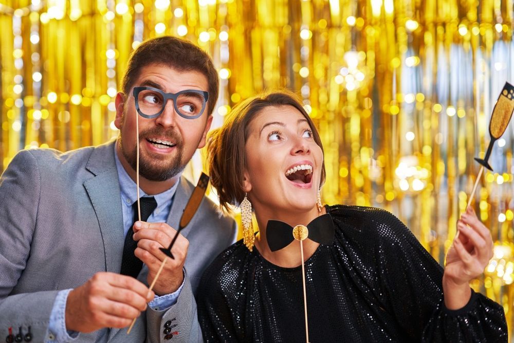 A man and a woman are holding photo booth props.