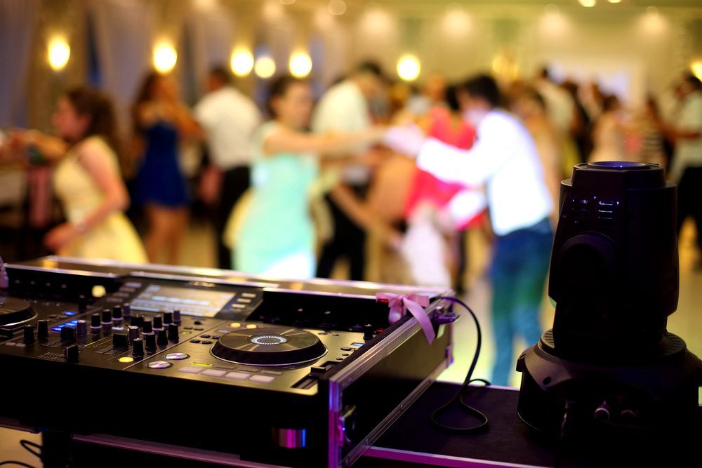 A dj is playing music at a party with people dancing in the background.