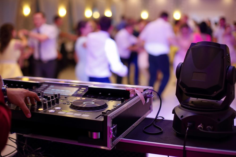 A dj is playing music at a party with people dancing in the background.
