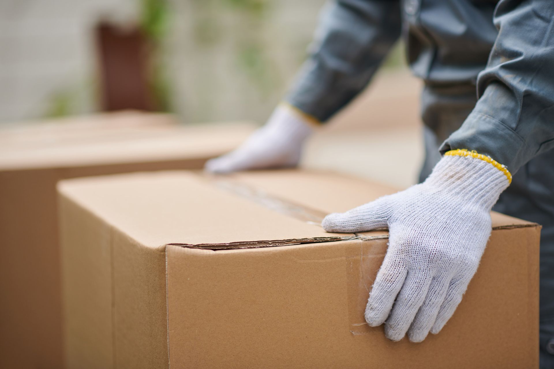 Gloved hands sealing a cardboard box in a warehouse setting