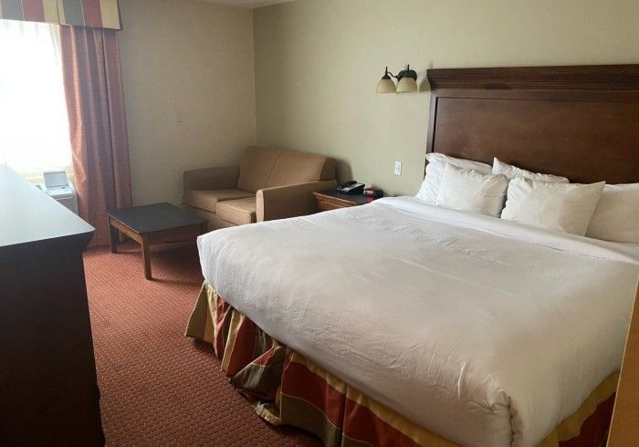 A hotel room with a king size bed , chair and dresser.