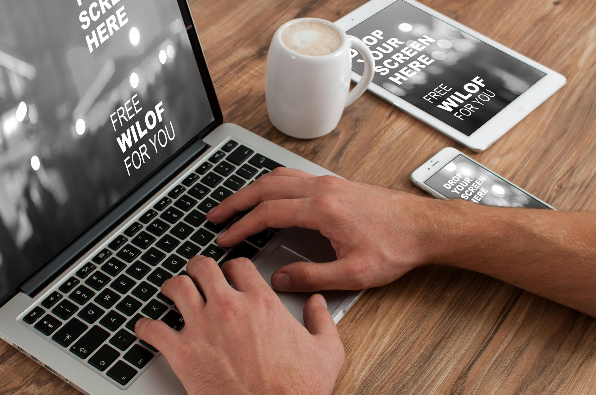 Hands typing on a laptop at a wooden desk with a coffee mug and notebook nearby.
