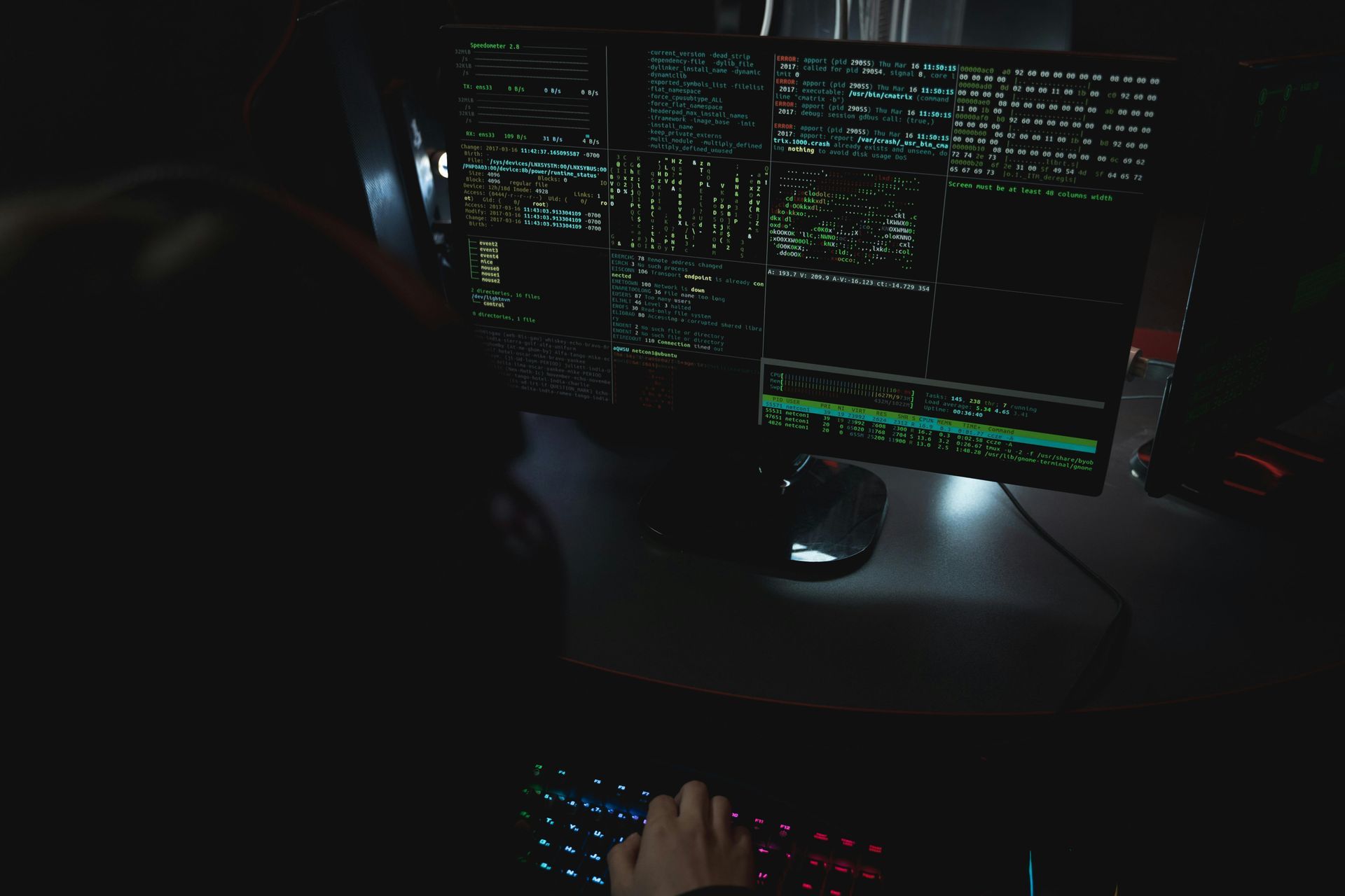 Person at a computer with multiple screens, in a dark room. Typing, displays code and graphs.