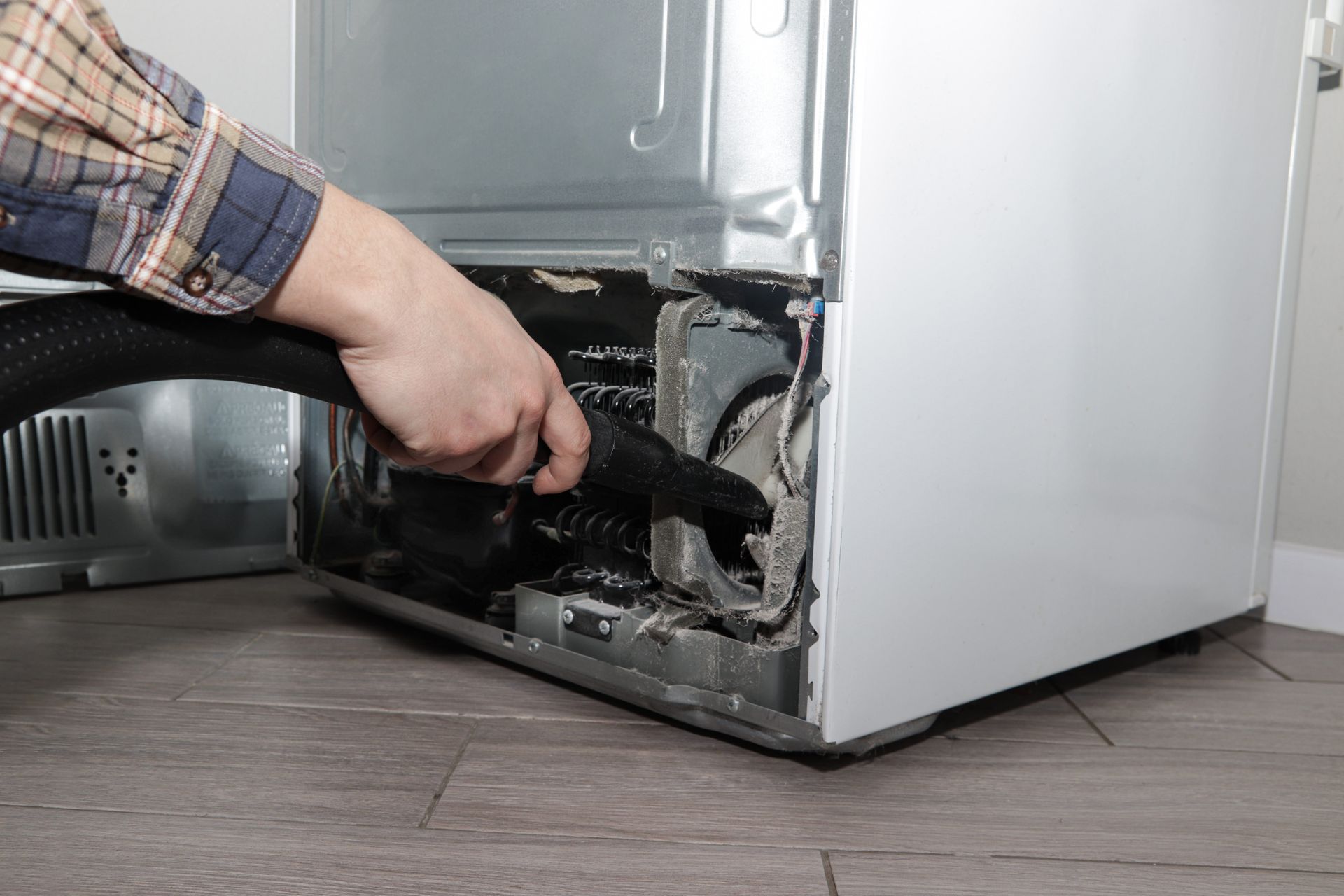Technician repairing a refrigerator compressor with a cordless drill and tools on the floor. Technician repairing a refrigerator at an appliance repair store