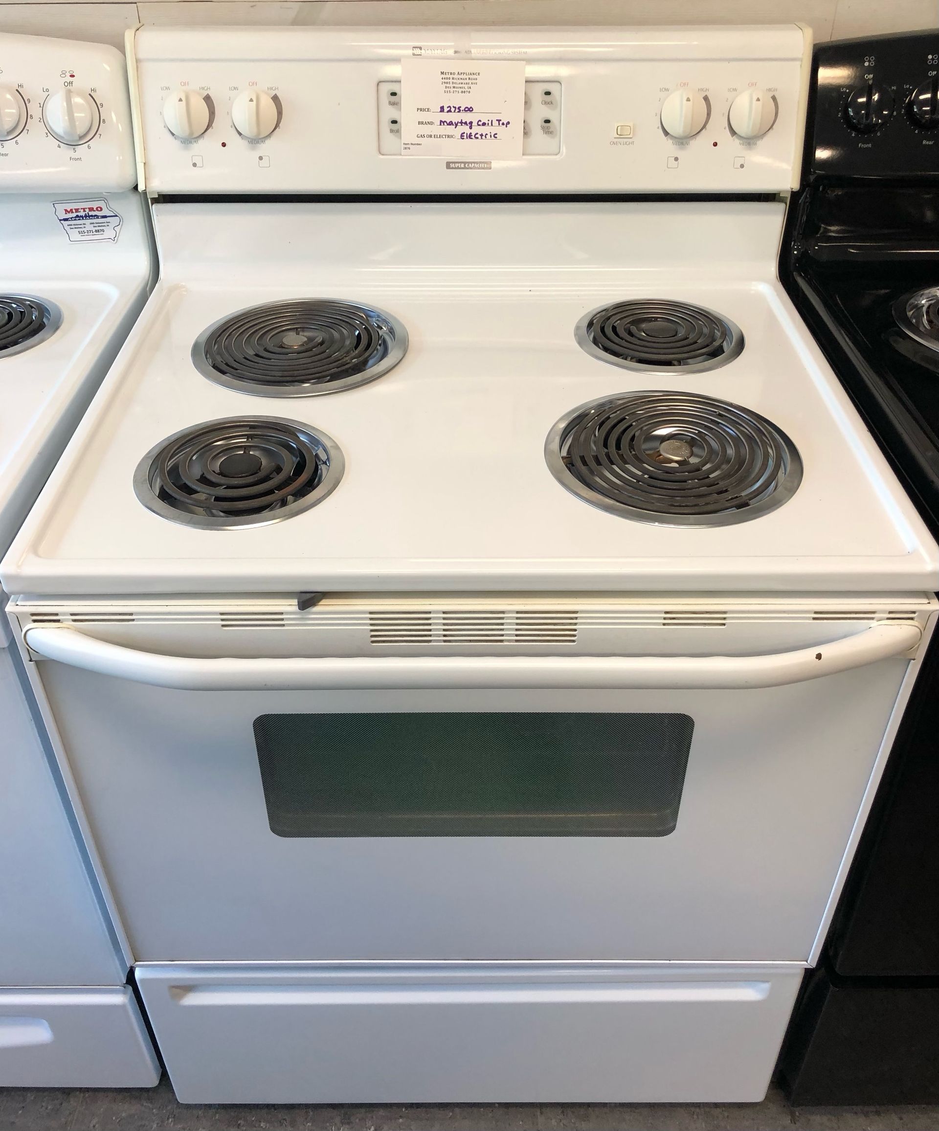 White electric stove with four coil burners and oven in a kitchen, flanked by other appliances.