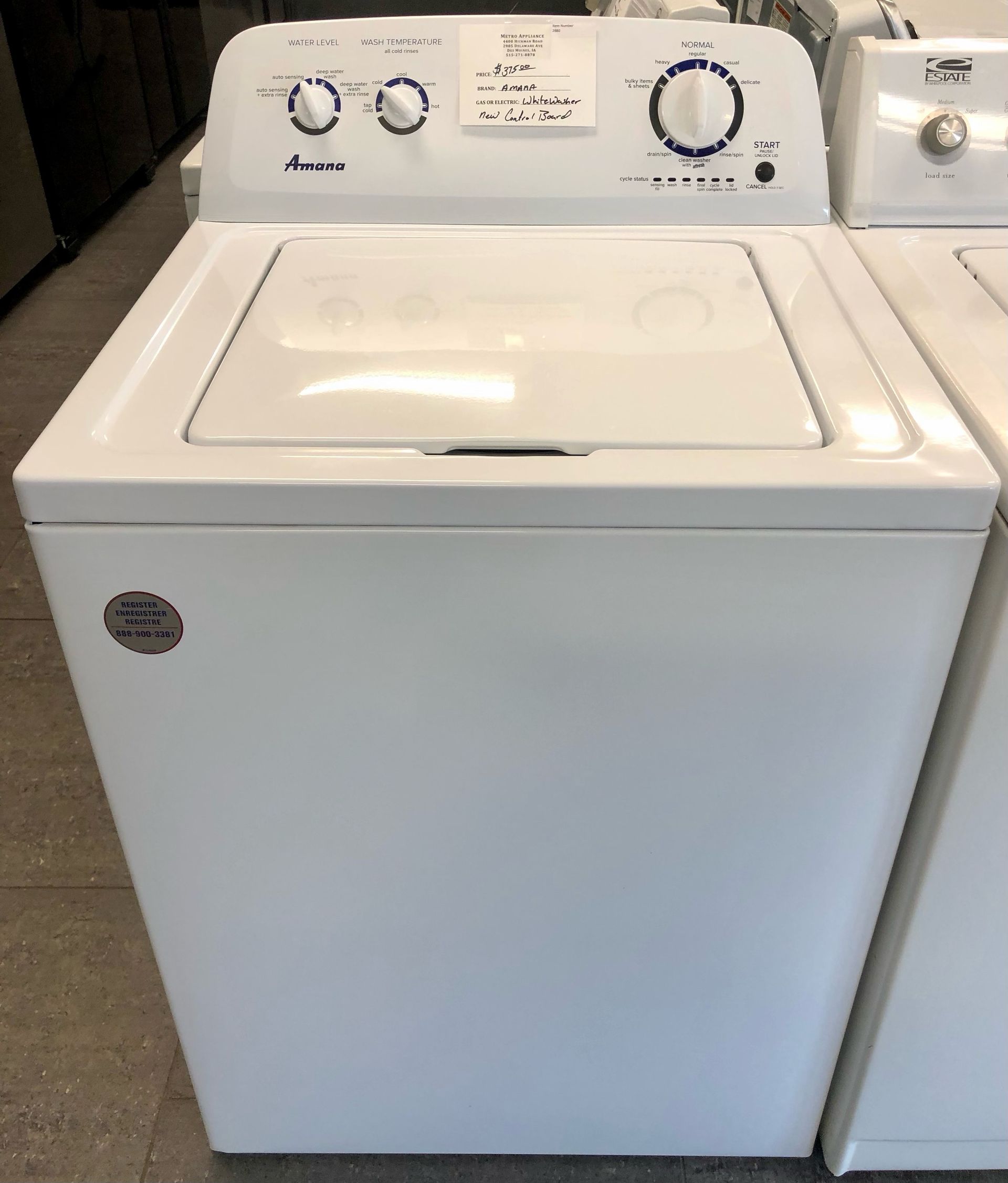White top-loading washing machine with white control panel and knobs in a laundry room.
