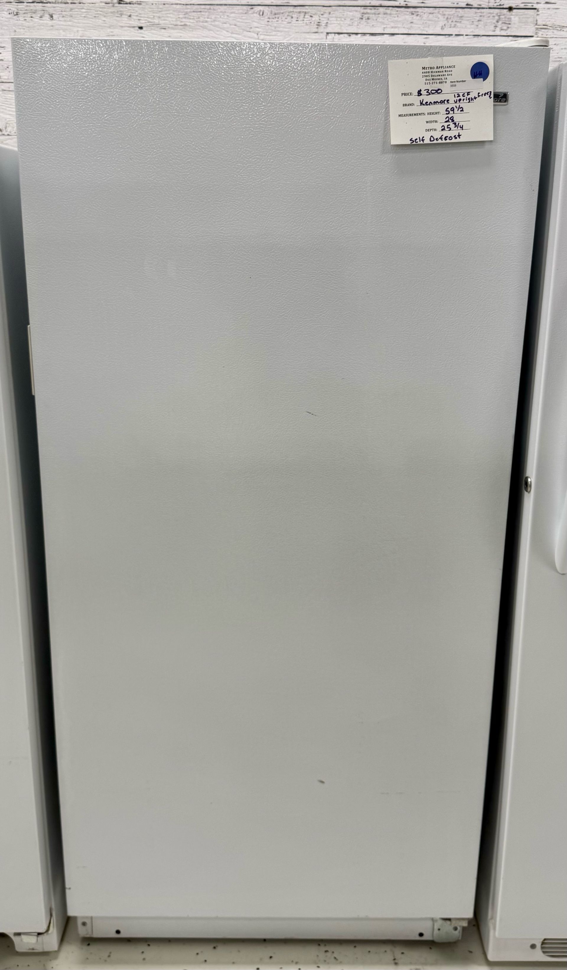 White upright freezer with a small label in the top-right corner, shown in a store aisle.