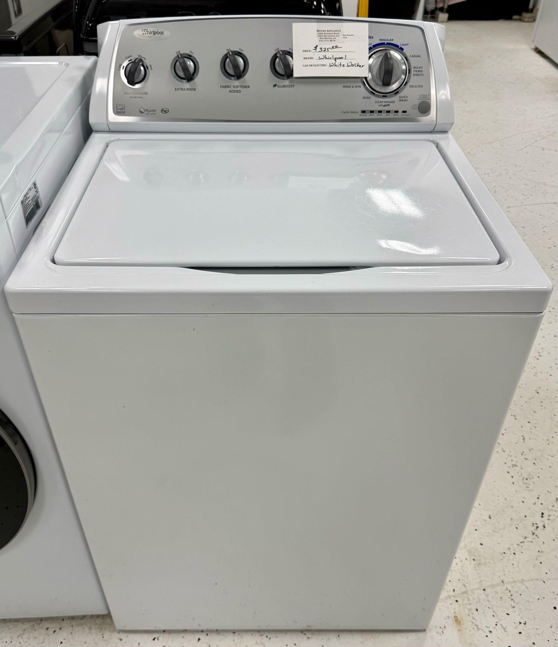 White top-loading washing machine with control knobs in a laundry store.