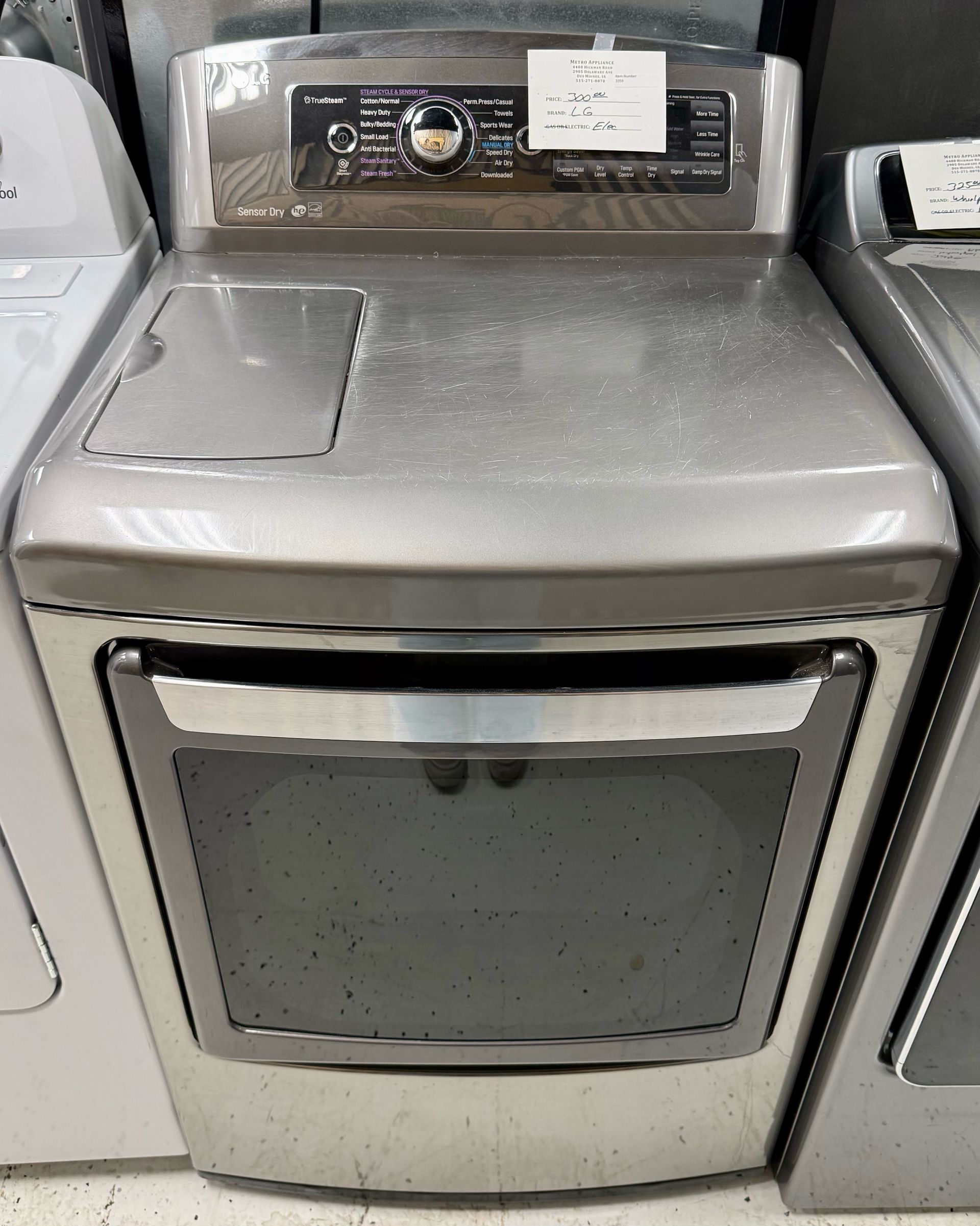 Stainless steel front-loading dryer with control panel, shown in an appliance store display.