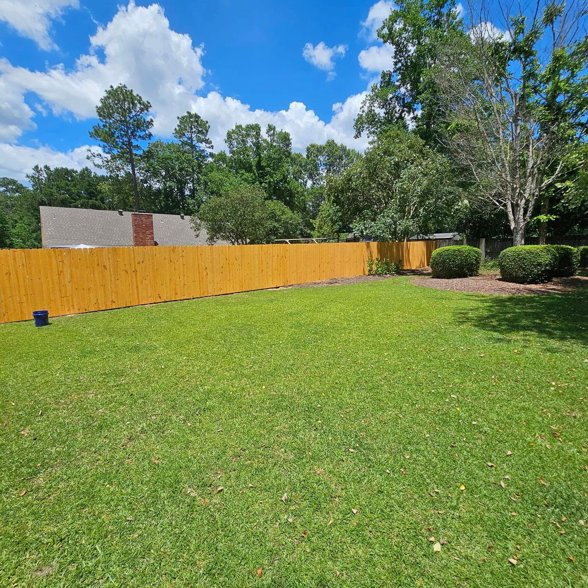 A wooden fence surrounds a large lush green yard.