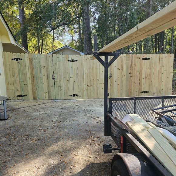 A wooden fence is being built next to a trailer filled with wood.