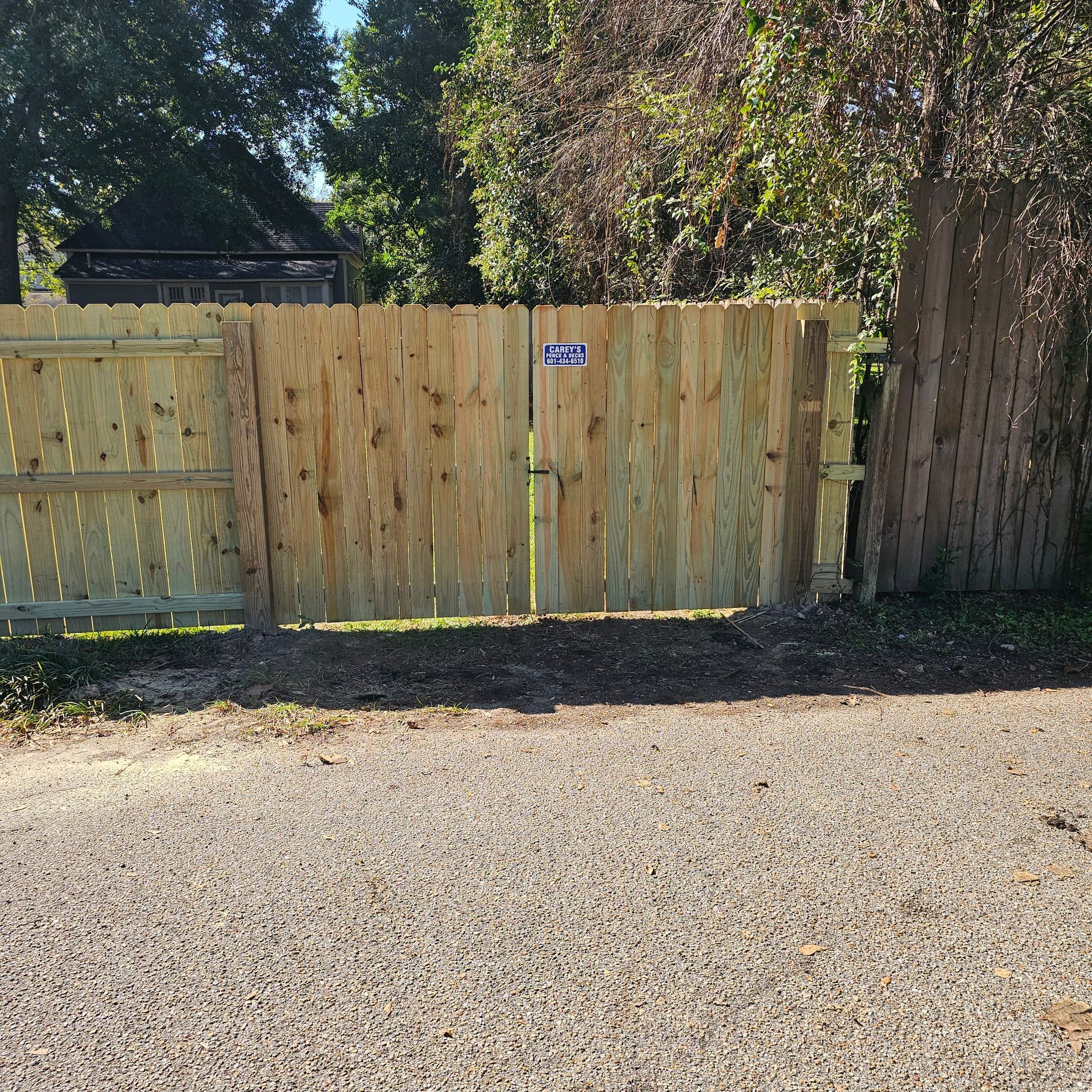 A wooden fence with a gate in the middle of a gravel driveway.