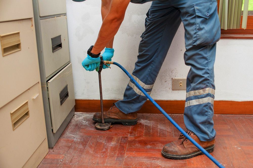 A Man is Standing on a Wooden Floor Holding a Hose — Territory Pest Control In Winnellie, NT