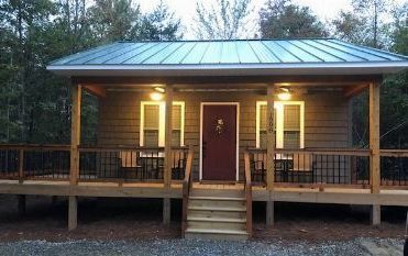 Front porch of a small wooden cabin with a metal roof, lit warmly at dusk.