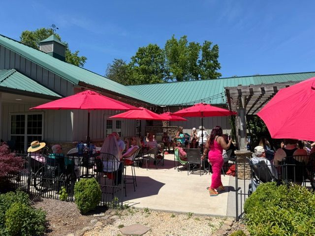 Outdoor café patio with red umbrellas, seated diners, and a green-roofed building under a clear blue sky