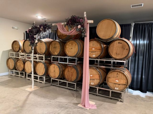 Rows of wooden wine barrels on metal racks in a cellar-like room with pink drapery and black curtains