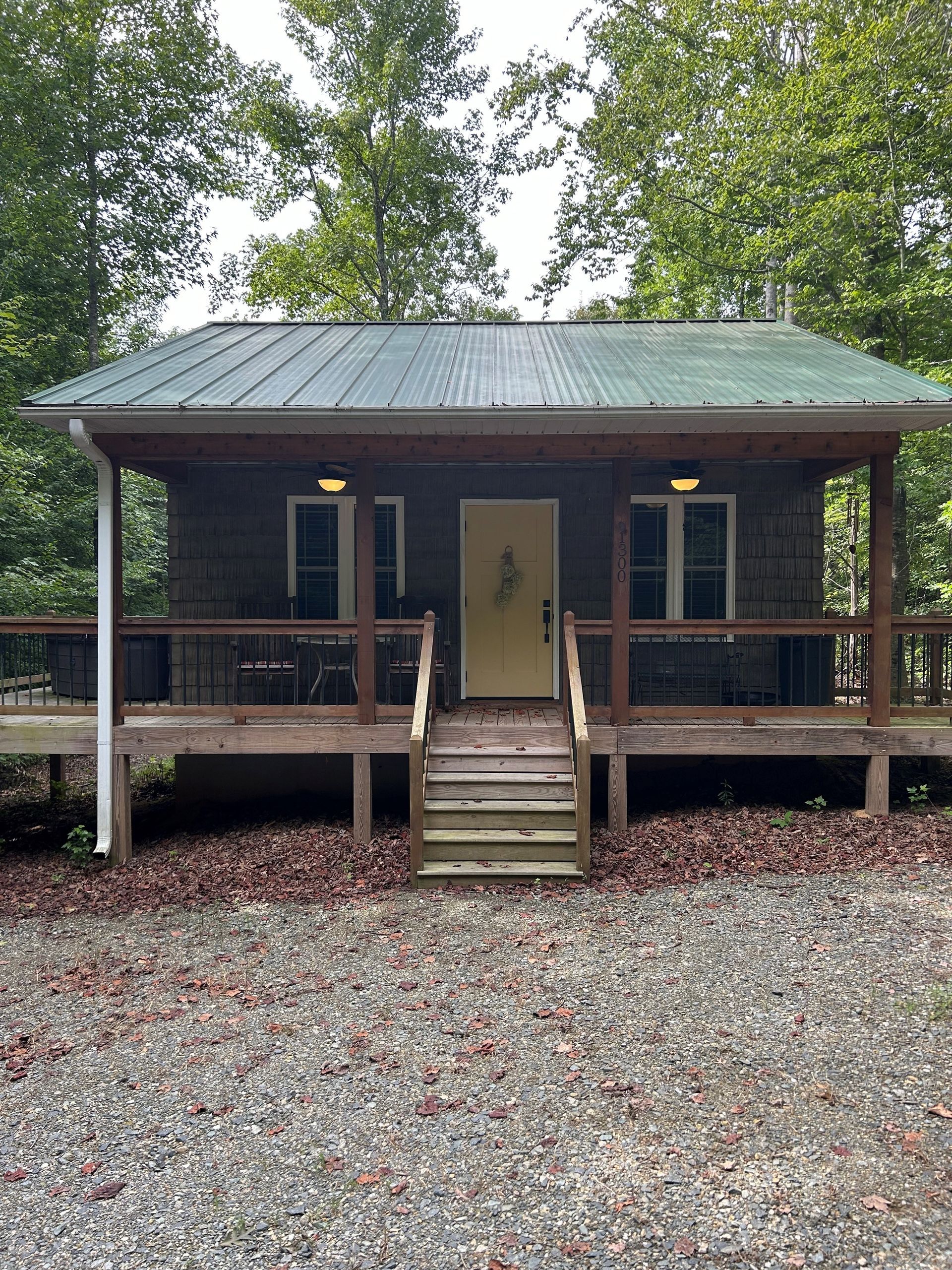 Small rustic cabin with a front porch, green metal roof, and wooden steps in a wooded setting.