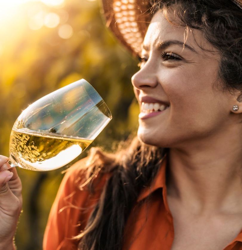 Smiling person holding a glass of white wine outdoors in warm sunlight