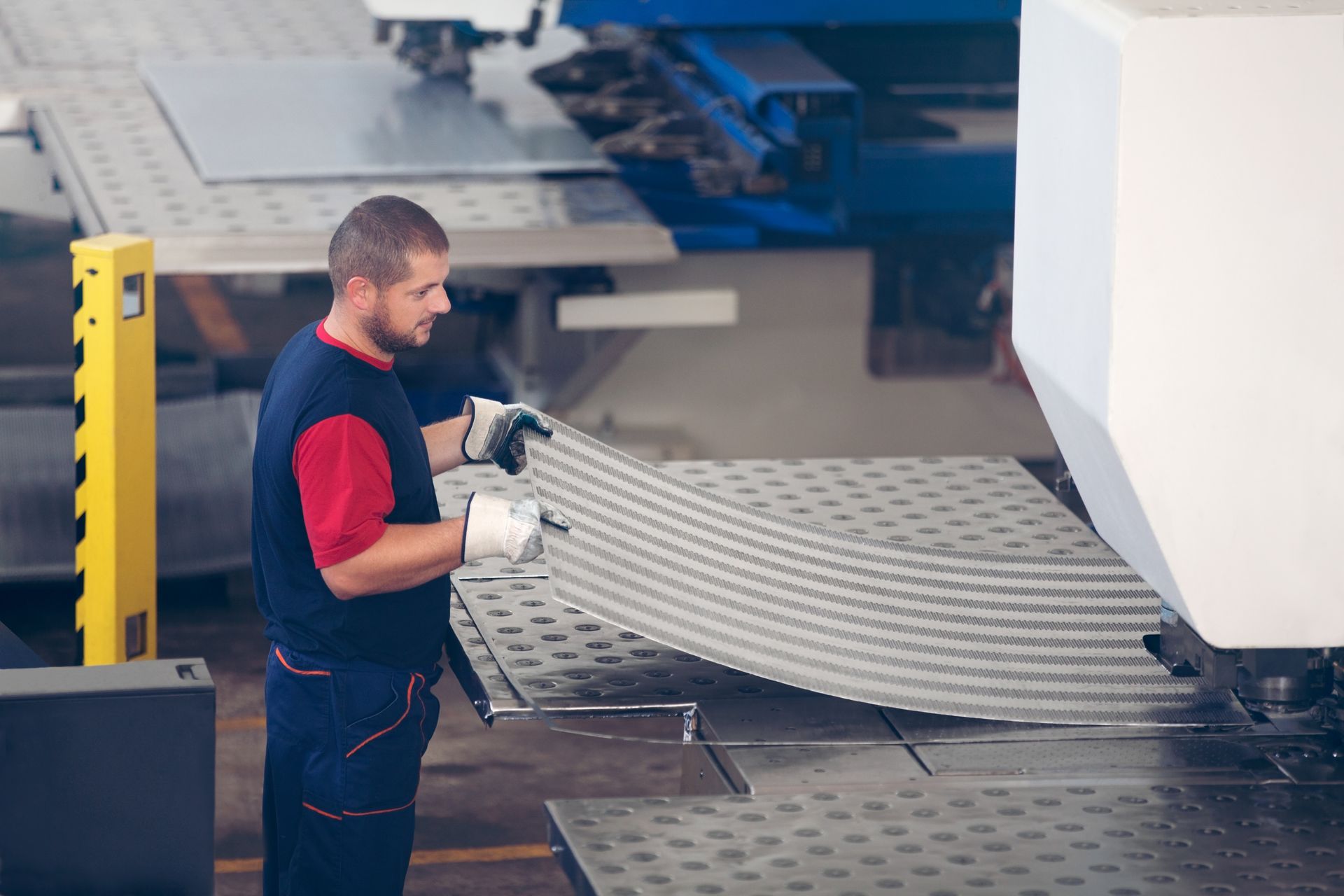 An industrial worker is in action on a metal press machine, holding a piece of steel.