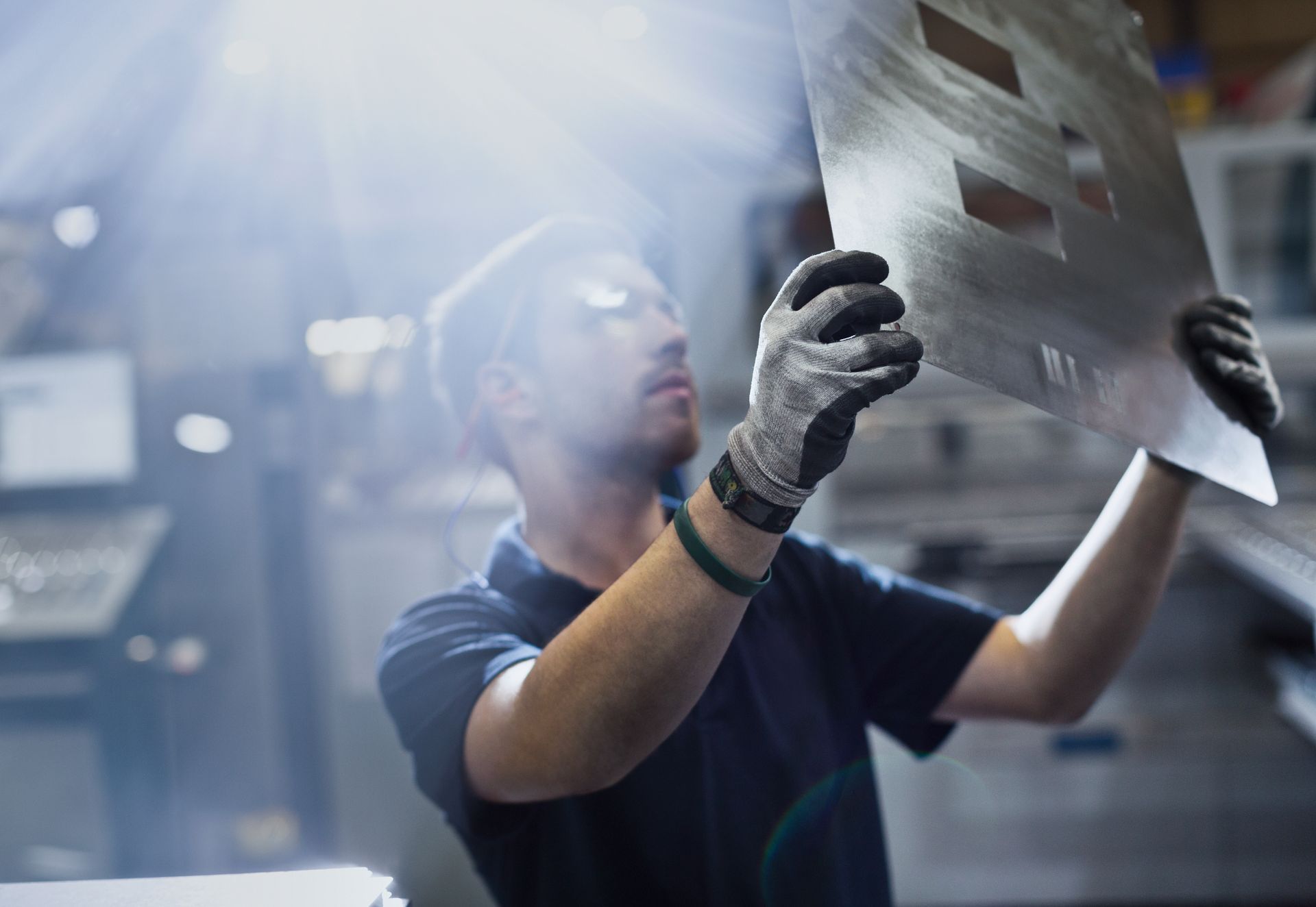 Factory worker examining a large metal sheet under bright industrial lighting.