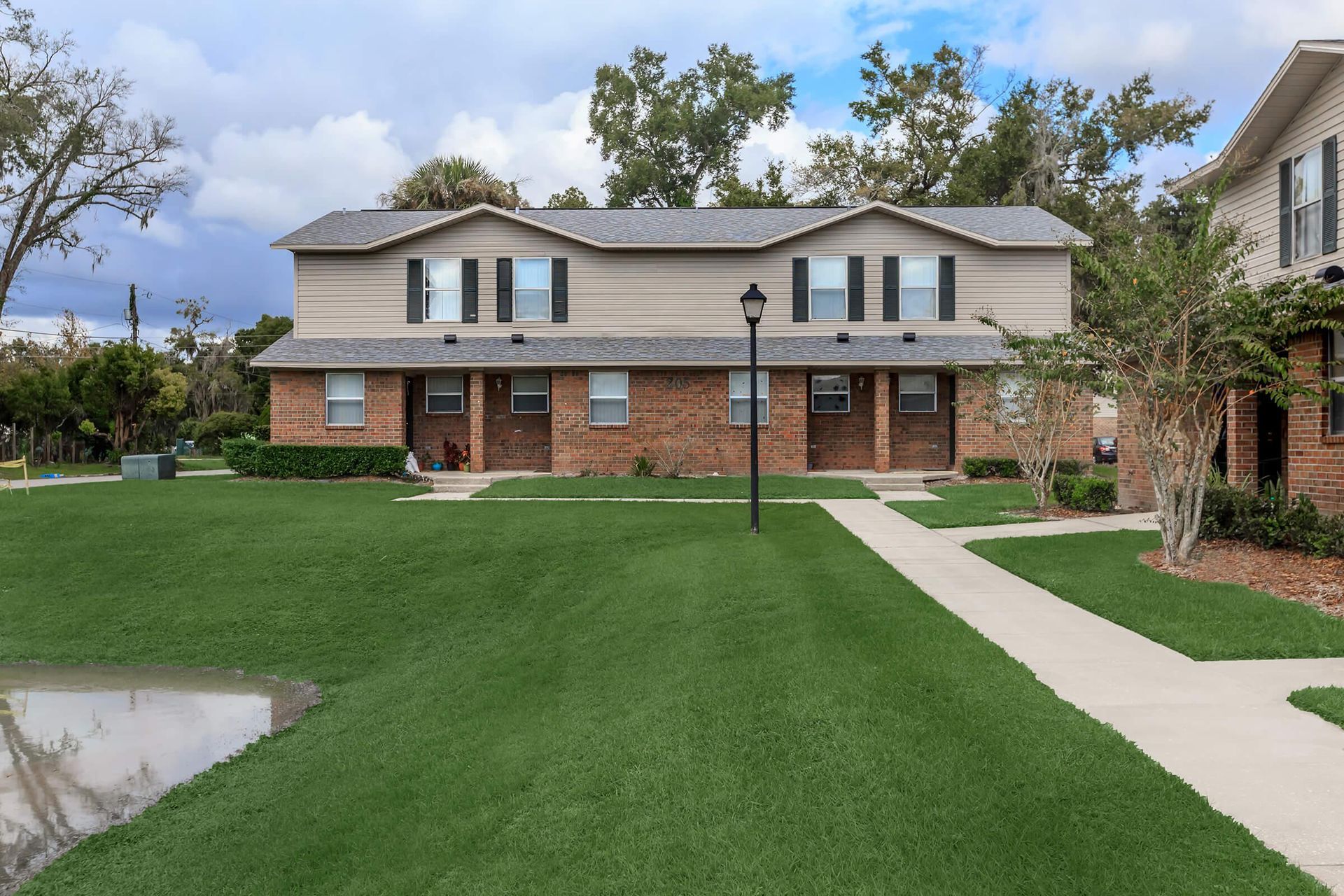 Two-story brick and beige apartment building with a green lawn and a sidewalk.