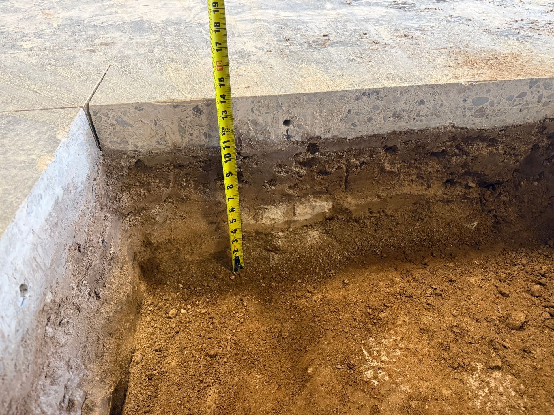 Measuring tape against a dug dirt trench beside a concrete edge