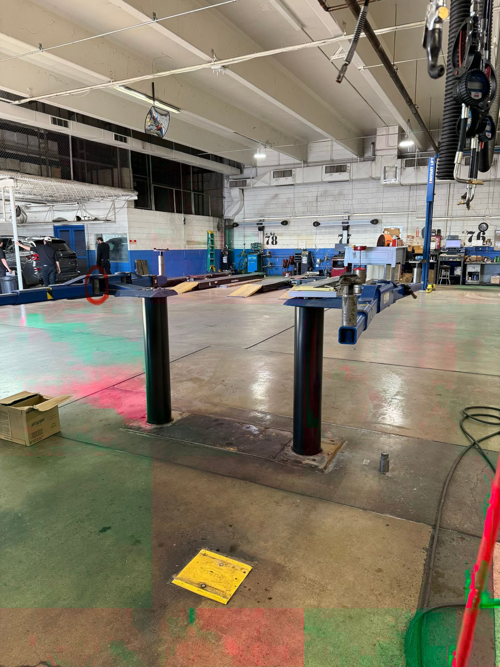 Indoor gym or workshop with equipment, blue chairs along the wall, and black posts on a worn floor.
