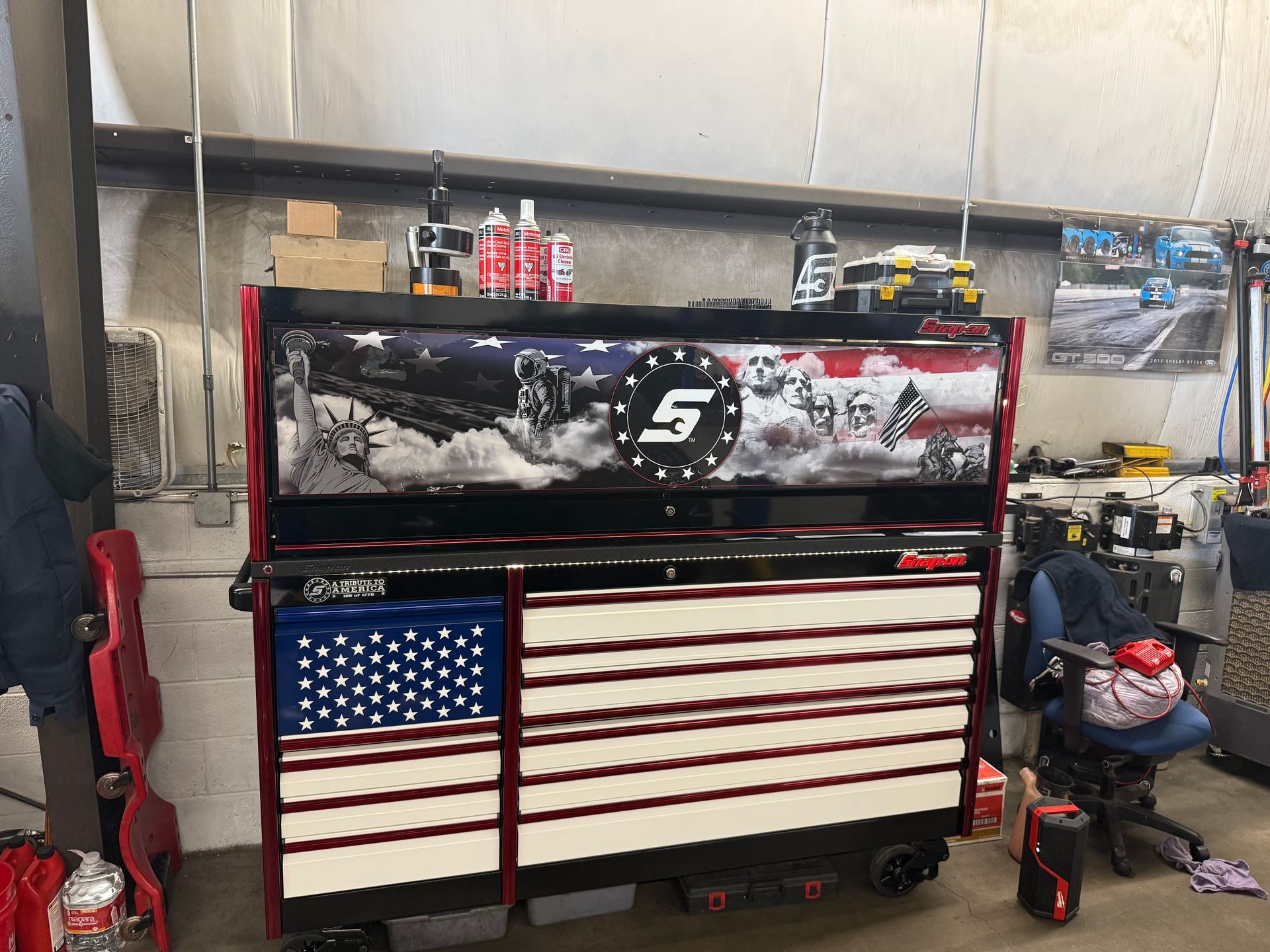 Red-and-black mechanic’s tool chest with an American flag design in a workshop, with tools on top.