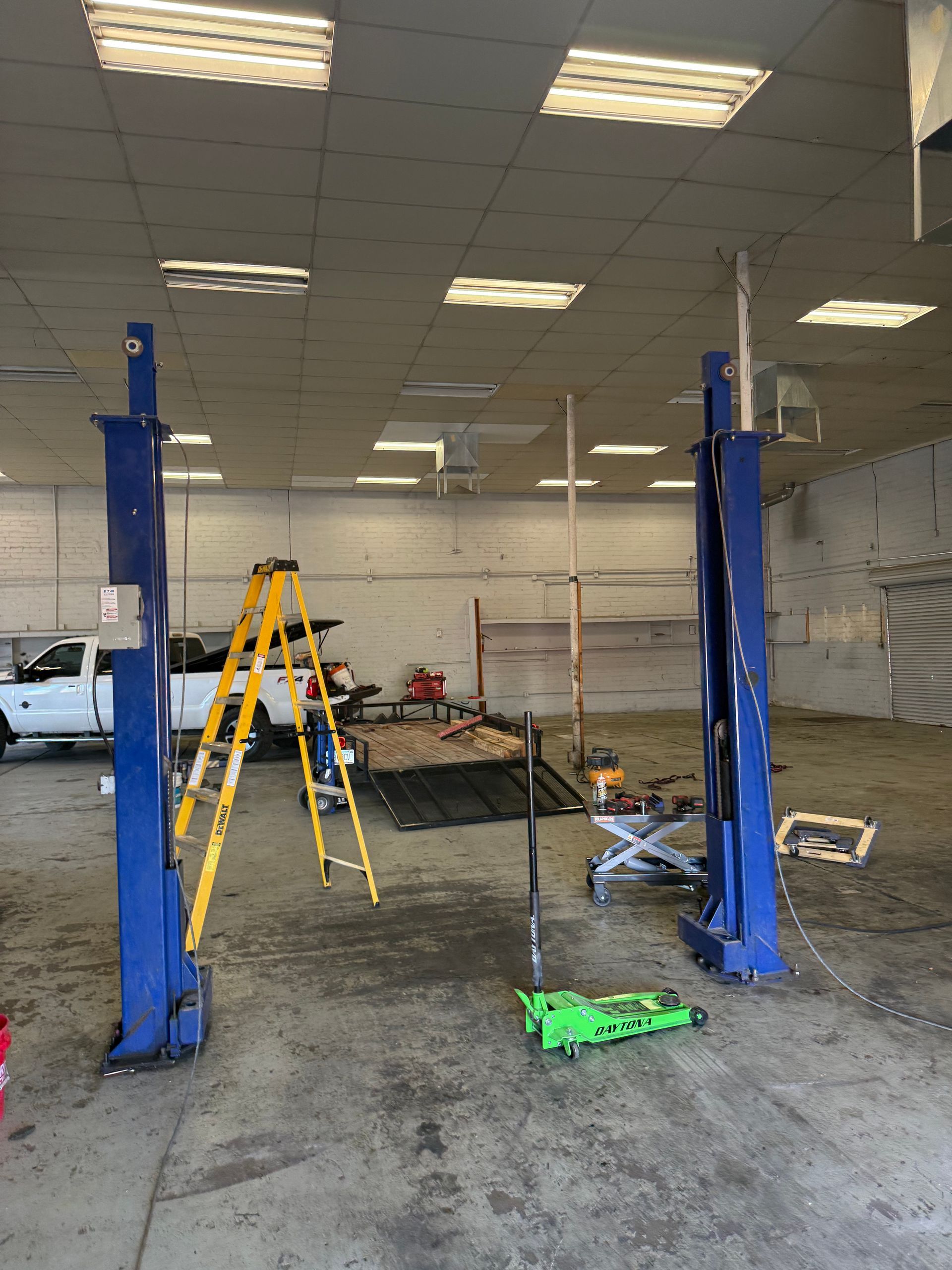 Auto repair shop with blue lift posts, yellow ladder, and equipment on a concrete floor